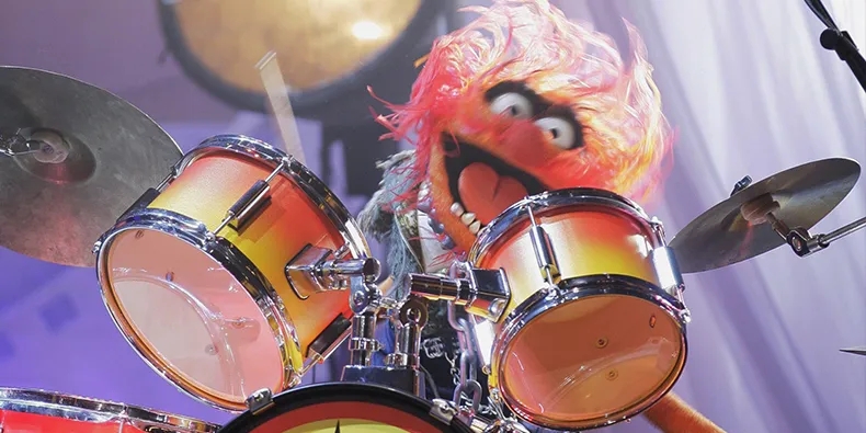 Animal from the muppets a full action photo with him hitting his drumset enthusiastically, eyes wide open, mouth open, orangy red hair flying. This drummer is in the zone people! 
